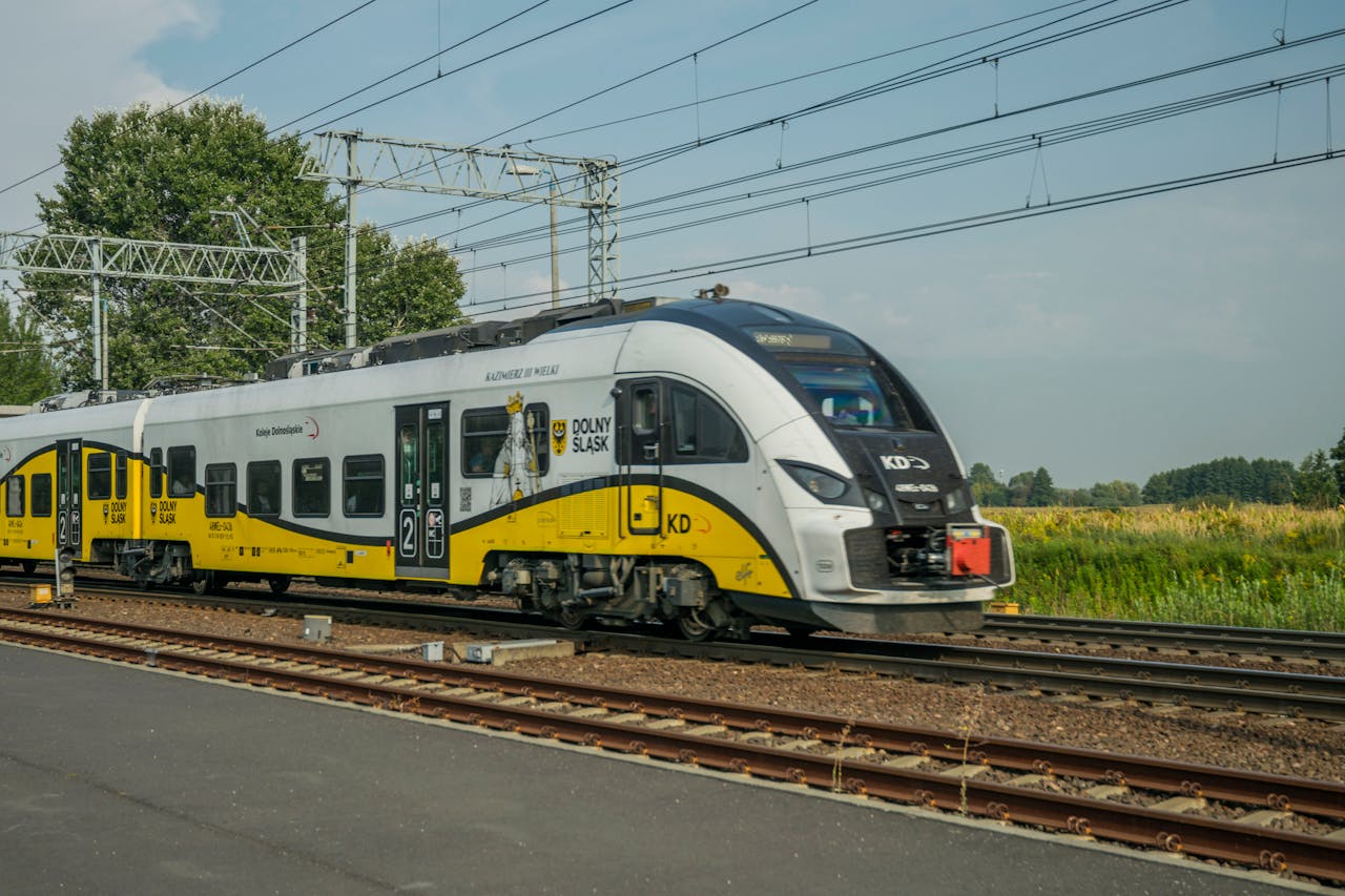 A sleek commuter train travels in Wrocław, Poland's scenic countryside on a sunny day.